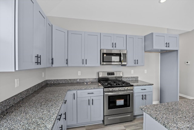 kitchen featuring dark stone counters, appliances with stainless steel finishes, light wood-type flooring, and gray cabinets