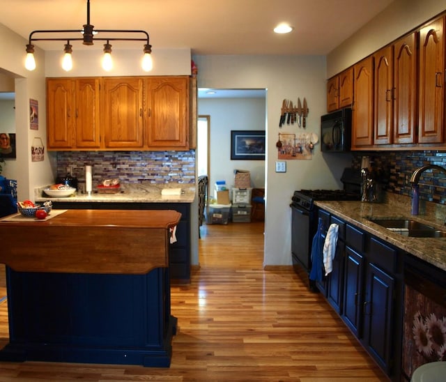 kitchen with black appliances, light wood-type flooring, light stone countertops, decorative backsplash, and sink