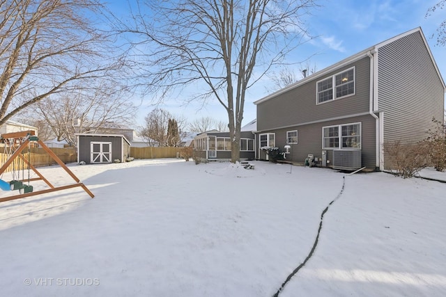 snow covered back of property with a playground, a sunroom, a shed, and central AC unit