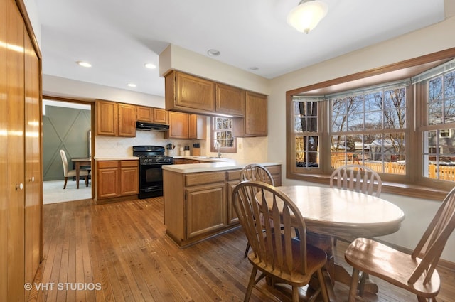 kitchen with kitchen peninsula, a wealth of natural light, black gas range oven, and dark hardwood / wood-style floors