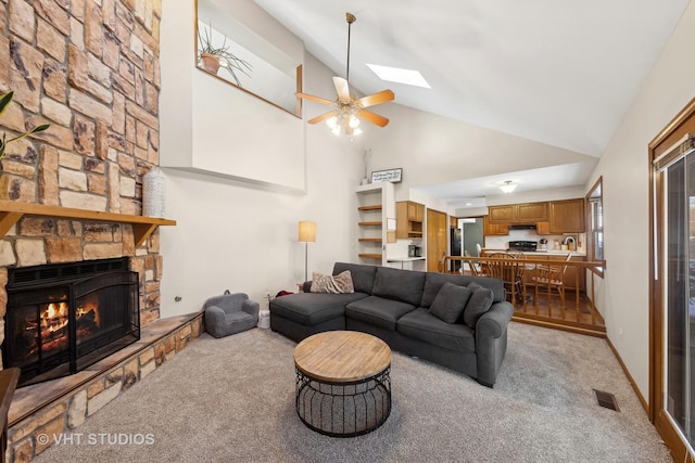 living room featuring lofted ceiling with skylight, a fireplace, ceiling fan, and light colored carpet