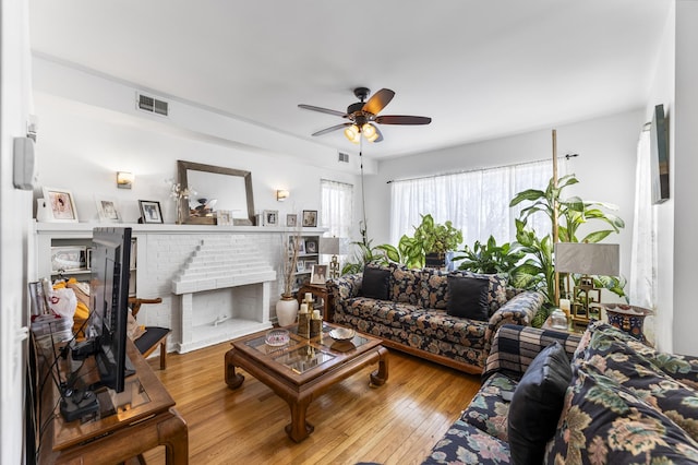 living room featuring a fireplace, ceiling fan, and light hardwood / wood-style floors