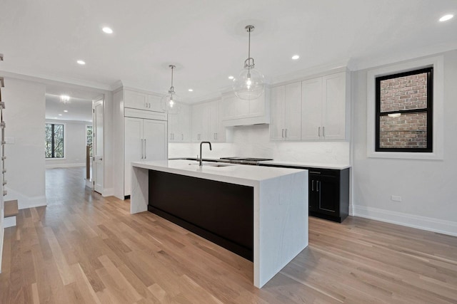 kitchen with white cabinets, pendant lighting, backsplash, and an island with sink