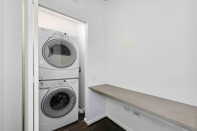 clothes washing area with dark wood-style floors, laundry area, stacked washing maching and dryer, and baseboards