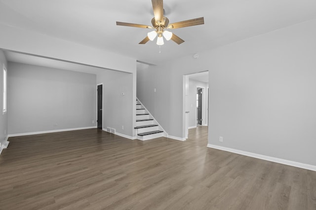 unfurnished living room featuring stairway, a ceiling fan, wood finished floors, and baseboards