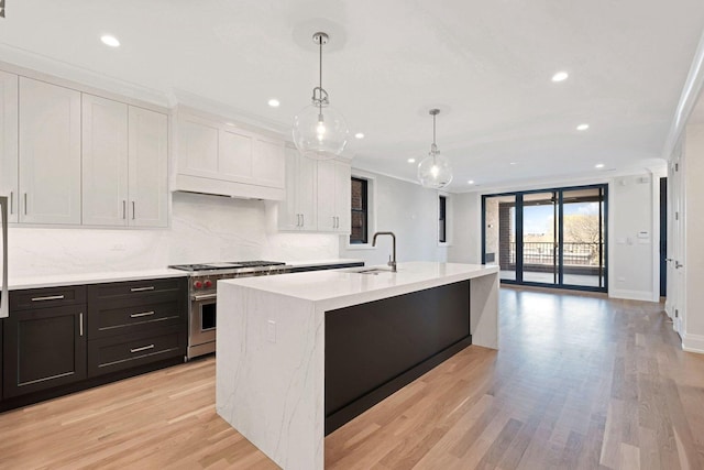 kitchen with white cabinetry, high end stainless steel range oven, ornamental molding, hanging light fixtures, and a kitchen island with sink