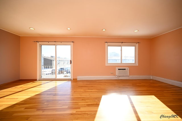 spare room featuring a healthy amount of sunlight, light hardwood / wood-style flooring, ornamental molding, and an AC wall unit