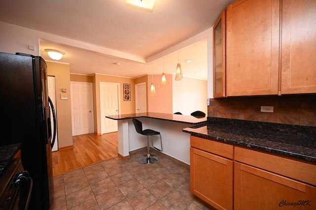 kitchen with black fridge, dark stone countertops, stove, backsplash, and pendant lighting