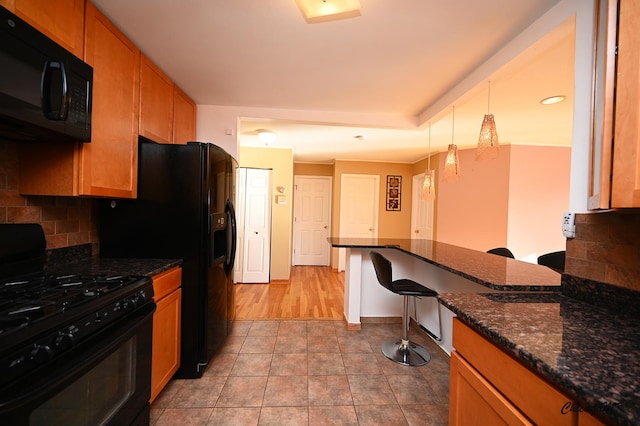 kitchen with black appliances, dark stone counters, pendant lighting, a kitchen bar, and decorative backsplash