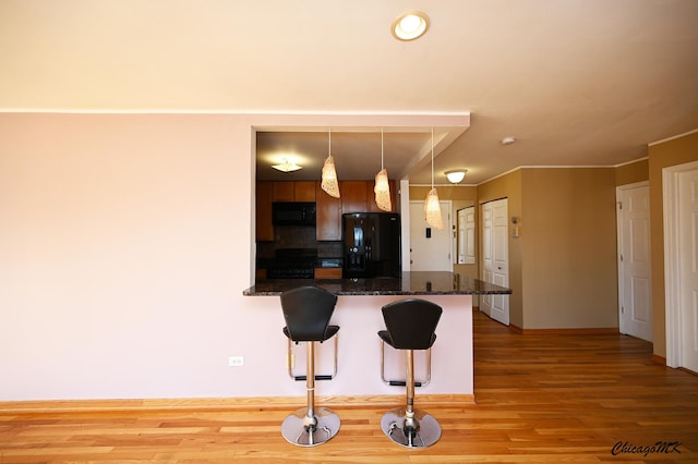 kitchen with decorative light fixtures, a kitchen bar, dark stone countertops, kitchen peninsula, and black appliances