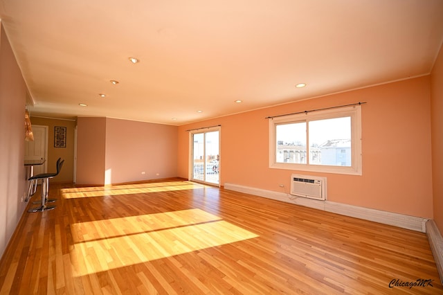 unfurnished living room with ornamental molding, a wall mounted AC, and light wood-type flooring