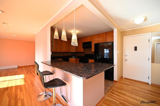 kitchen featuring black fridge with ice dispenser, decorative light fixtures, stove, kitchen peninsula, and a breakfast bar area