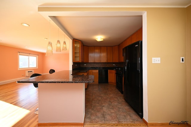 kitchen with kitchen peninsula, hanging light fixtures, black appliances, a breakfast bar area, and dark stone countertops