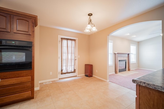 kitchen featuring an inviting chandelier, black oven, a multi sided fireplace, pendant lighting, and light colored carpet