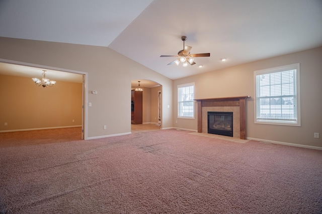 unfurnished living room featuring ceiling fan with notable chandelier, vaulted ceiling, a tile fireplace, and carpet