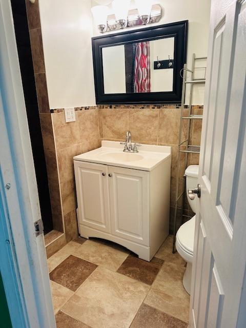 bathroom featuring toilet, vanity, and tile walls