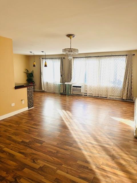 unfurnished room with wood-type flooring, an AC wall unit, and a notable chandelier