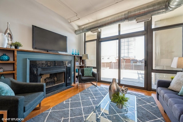 living room with floor to ceiling windows, a tiled fireplace, and wood-type flooring