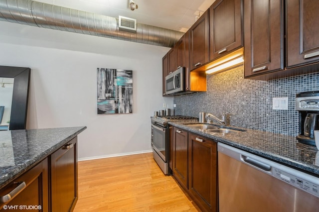 kitchen with appliances with stainless steel finishes, dark stone counters, decorative backsplash, sink, and light hardwood / wood-style flooring