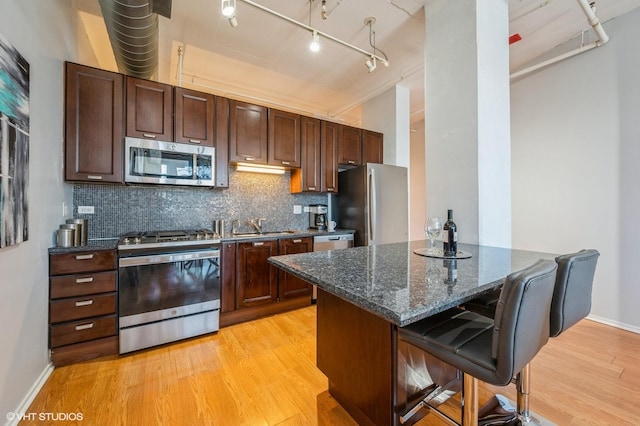 kitchen with dark stone countertops, light hardwood / wood-style flooring, backsplash, a breakfast bar, and appliances with stainless steel finishes