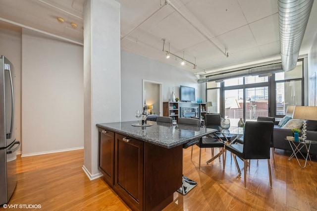 kitchen featuring rail lighting, light wood-type flooring, dark stone counters, stainless steel fridge, and dark brown cabinetry