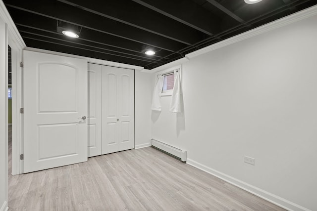 basement with a baseboard heating unit, light hardwood / wood-style flooring, and ornamental molding