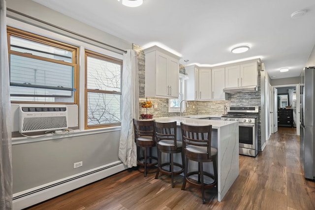 kitchen featuring a kitchen bar, kitchen peninsula, stainless steel appliances, a baseboard radiator, and white cabinets