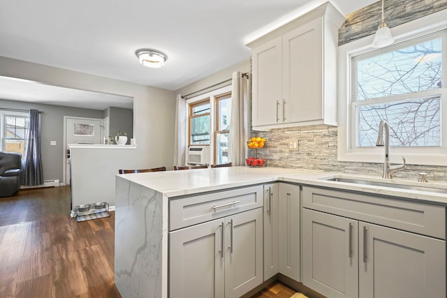 kitchen featuring backsplash, dark hardwood / wood-style floors, kitchen peninsula, sink, and hanging light fixtures