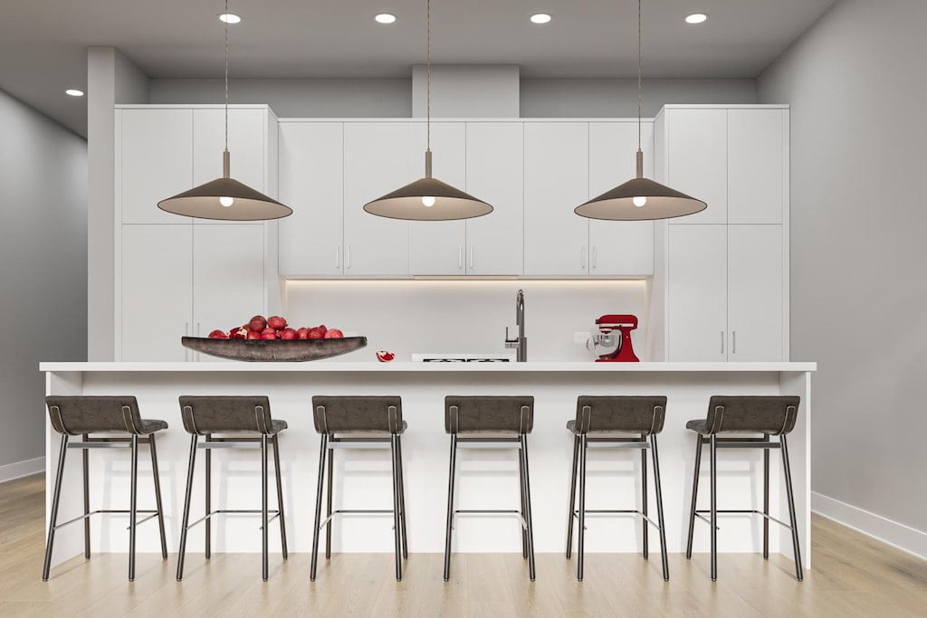 kitchen with white cabinets, light hardwood / wood-style floors, a kitchen island with sink, and a breakfast bar area