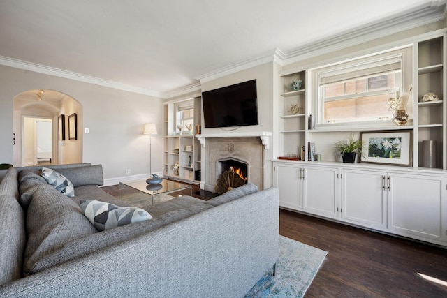 living room with built in shelves, dark hardwood / wood-style floors, crown molding, and a fireplace