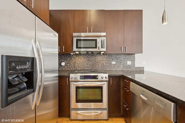 kitchen featuring appliances with stainless steel finishes, hanging light fixtures, dark stone counters, decorative backsplash, and kitchen peninsula