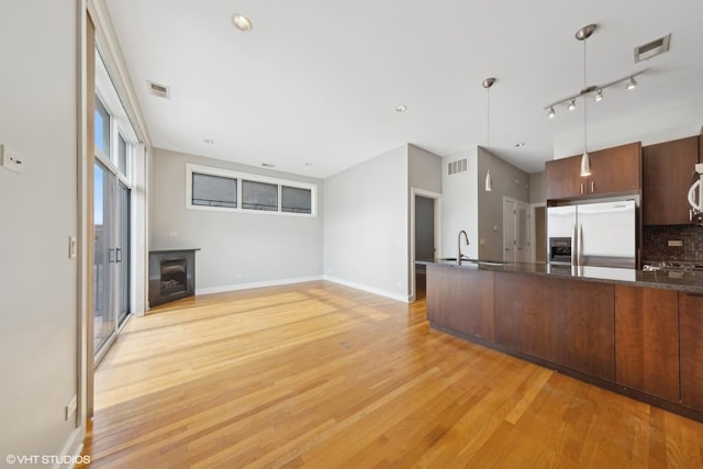 kitchen with sink, backsplash, stainless steel refrigerator with ice dispenser, pendant lighting, and light hardwood / wood-style floors