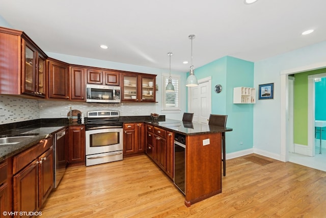 kitchen featuring decorative light fixtures, stainless steel appliances, dark stone counters, and light wood-type flooring