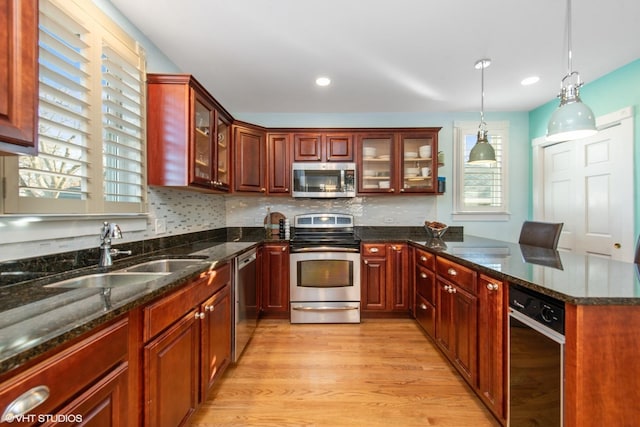 kitchen with decorative light fixtures, sink, dark stone countertops, light hardwood / wood-style floors, and stainless steel appliances