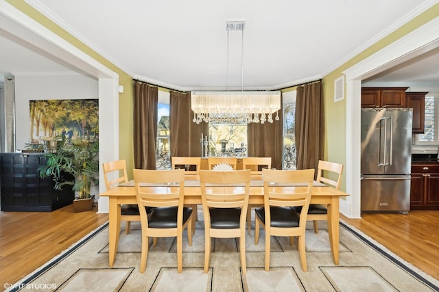 dining space featuring crown molding, an inviting chandelier, and light hardwood / wood-style flooring