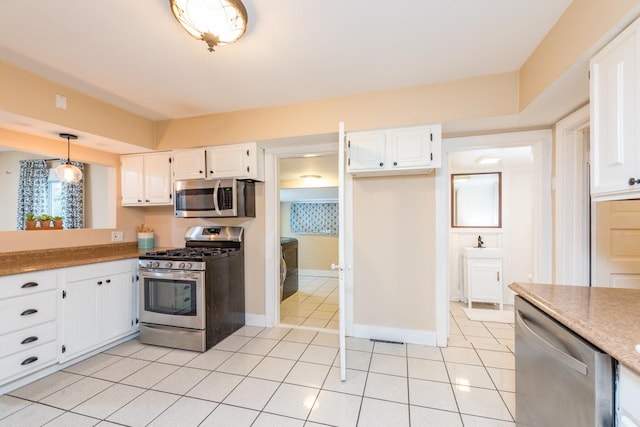 kitchen with hanging light fixtures, appliances with stainless steel finishes, light tile patterned flooring, and white cabinetry