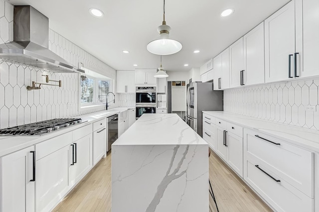 kitchen with appliances with stainless steel finishes, white cabinetry, hanging light fixtures, and wall chimney range hood