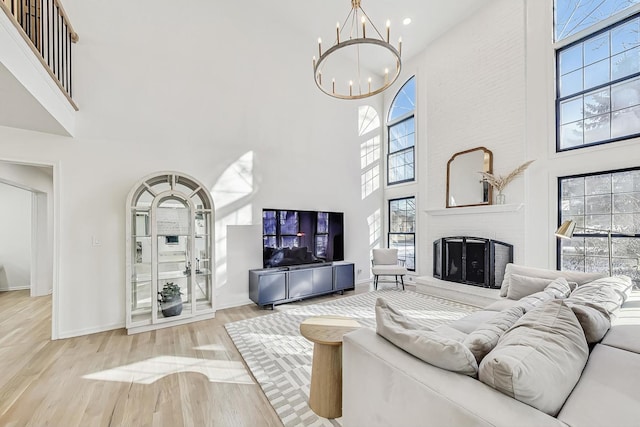 living room with light wood-type flooring, a towering ceiling, a large fireplace, and a chandelier