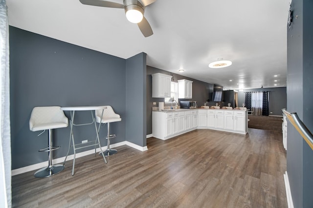 kitchen featuring kitchen peninsula, dark hardwood / wood-style floors, a breakfast bar, white cabinets, and ceiling fan