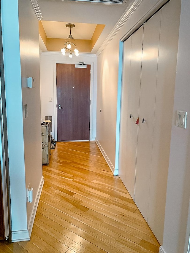 hall with an inviting chandelier, a tray ceiling, crown molding, and light hardwood / wood-style flooring