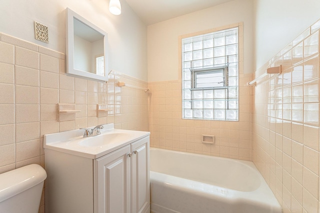 bathroom featuring tile walls, a tub to relax in, vanity, and toilet