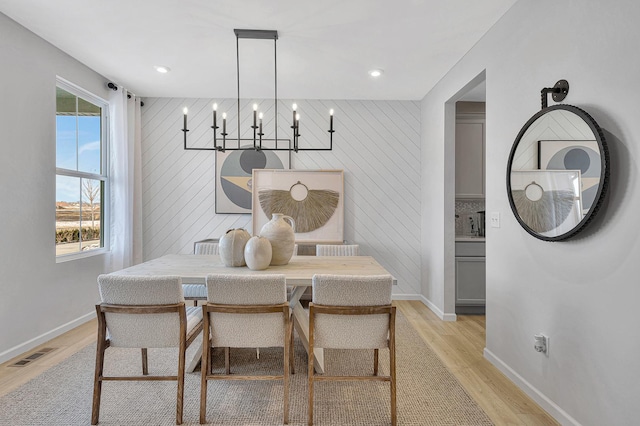 dining space featuring light hardwood / wood-style flooring, wooden walls, and a chandelier