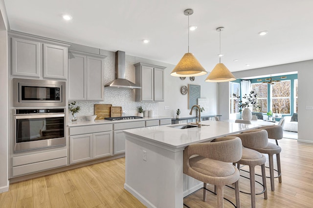 kitchen featuring pendant lighting, stainless steel appliances, wall chimney range hood, gray cabinets, and sink