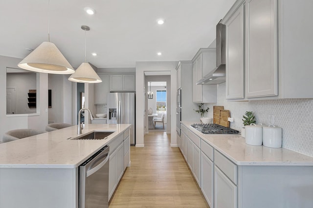 kitchen with a kitchen island with sink, appliances with stainless steel finishes, pendant lighting, wall chimney exhaust hood, and sink