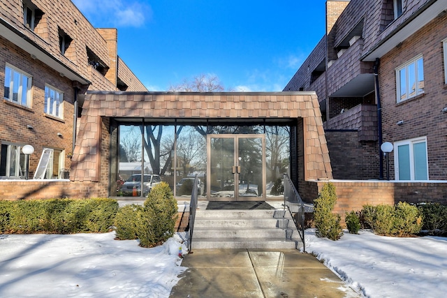 snow covered property entrance with french doors and brick siding