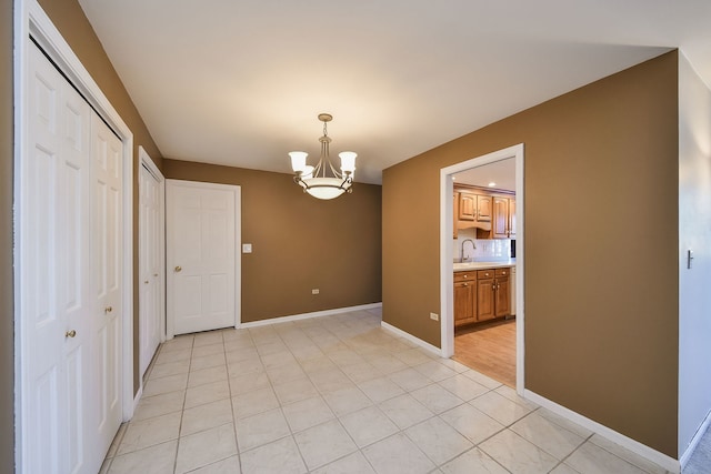 unfurnished dining area with light tile patterned flooring, a notable chandelier, baseboards, and a sink