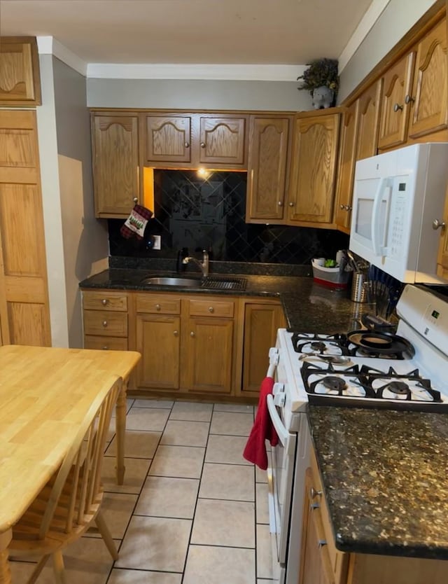 kitchen with white appliances, light tile patterned floors, backsplash, dark stone countertops, and sink