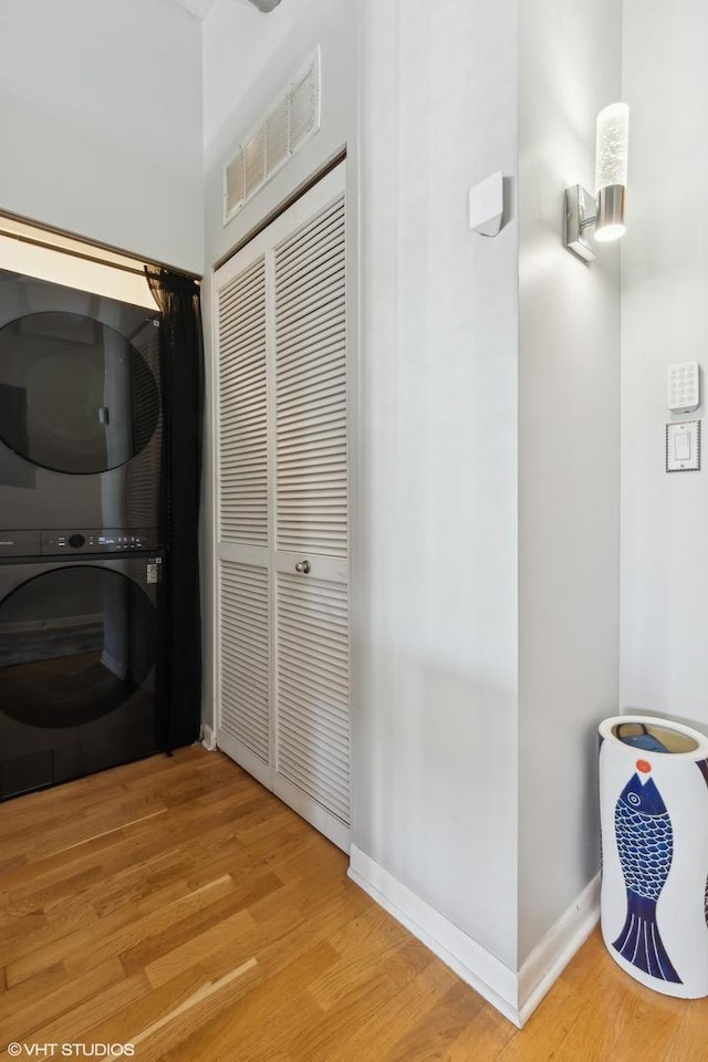 laundry room with stacked washing maching and dryer and light hardwood / wood-style floors