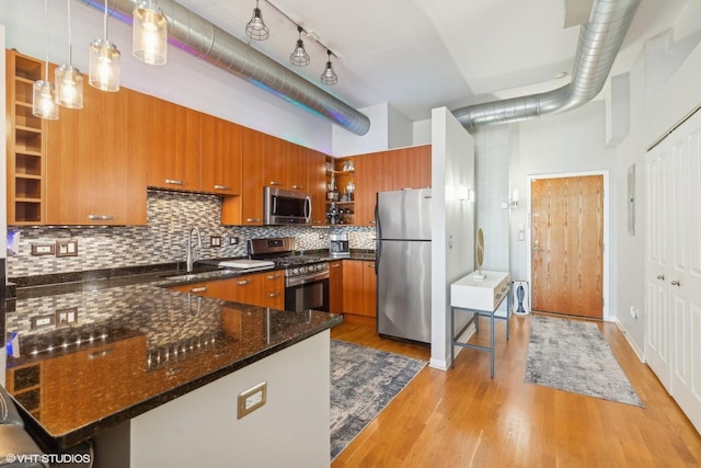 kitchen with appliances with stainless steel finishes, decorative light fixtures, dark stone counters, sink, and light wood-type flooring