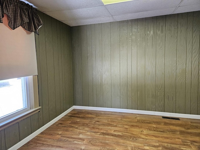 spare room with hardwood / wood-style floors, a drop ceiling, and wooden walls